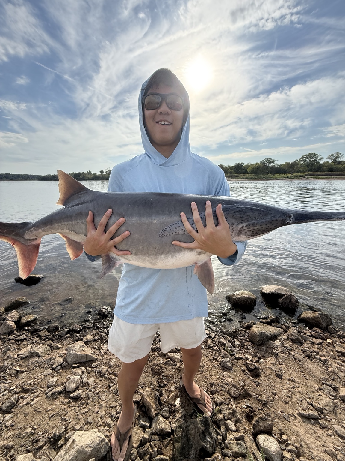 Angler holding a paddlefish on the shoreline